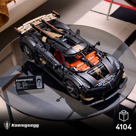 Grijze, gedetailleerde LEGO-auto met oranje interieur en gouden accenten, op een glazen tafel. "Koenigsegg" label.