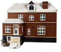 LEGO-huis met bruine bakstenen, witte dakranden, schoorsteen en sneeuw, met een figuur liggend buiten.