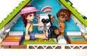 Twee vriendinnen in een LEGO huisje, één met roze pet, zittend op een groen kleed met op de achtergrond een raam met zend-signalen.