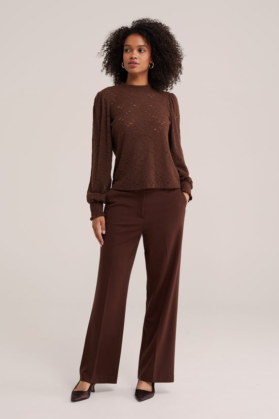 Model staand in bruine kanten top met pofmouwen en wijde bruine broek.