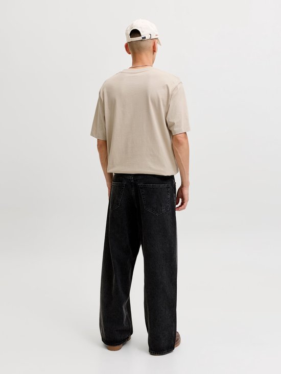 Man van achteren, met beige T-shirt met "ORIGINALS" opdruk, zwart jeans en pet.