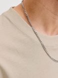 Close-up van een beige T-shirt met een zilveren ketting om de nek.