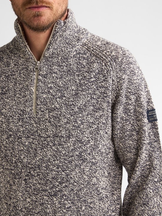 Close-up van een gemêleerde blauw-witte trui met rits en logo op de mouw.