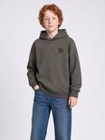 Jongen met krullend rood haar, met handen in de zakken, in een donkergroene hoodie en blauwe jeans.