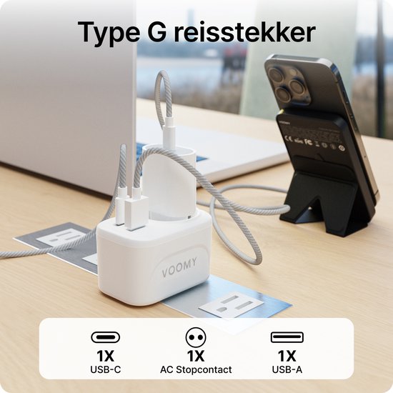 Witte Voomy reisadapter Type G aangesloten op een stopcontact, laadt een iPhone op. Met 1x USB-C, 1x AC stopcontact, 1x USB-A.