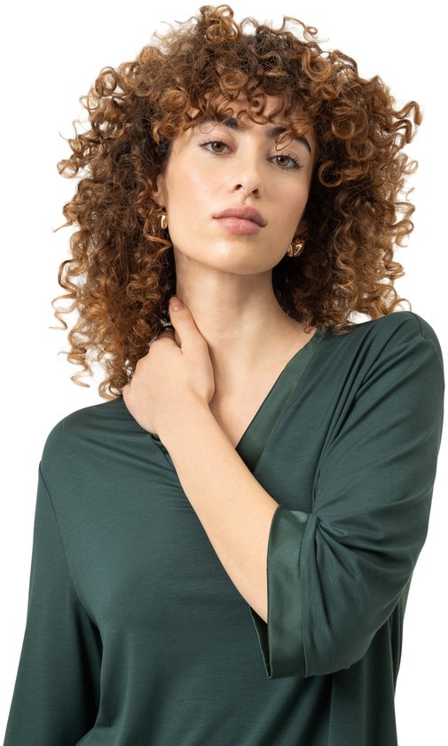 Model met krullend haar draagt een groen T-shirt met V-hals en satijnen detail op de mouw.