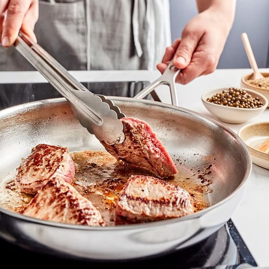Bovenaf, ingrediënten worden gebakken in een koekenpan, terwijl stukken vlees worden toegevoegd.