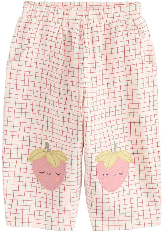 Witte broek met rood ruitjespatroon en applicaties van roze aardbeien met gesloten oogjes op de knieën.