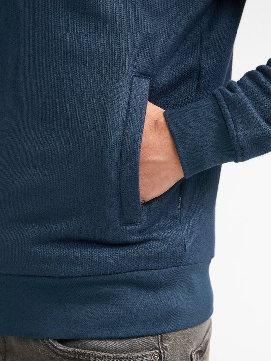 Detail van de zak van een blauw vest met geribde zoom en mouwboorden.