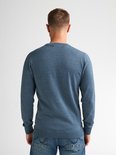 De achterkant van een man in een blauwe, fijngebreide trui en spijkerbroek.