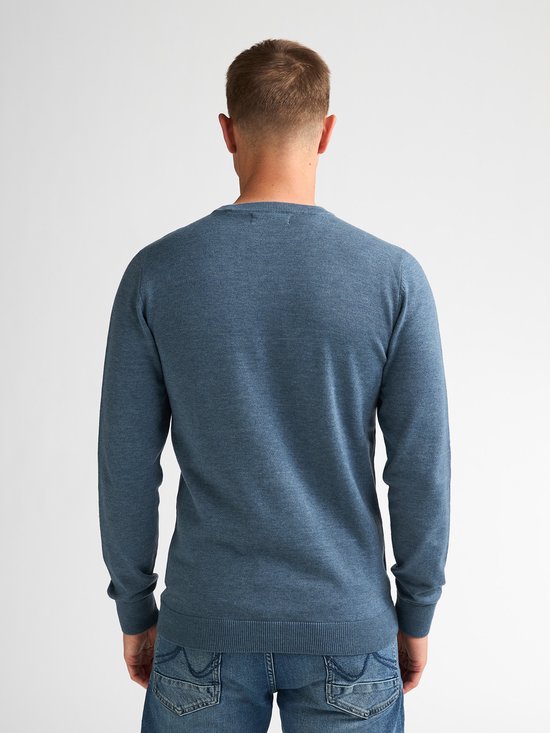 De achterkant van een man in een blauwe, fijngebreide trui en spijkerbroek.