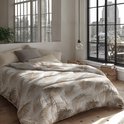 Dekbed met een beige palmbladerenprint op een crèmekleurige achtergrond, opgemaakt op een bed met uitzicht op een stad.