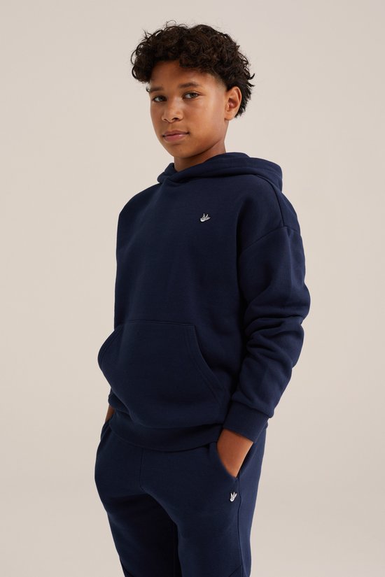 Jongen met donkerblauwe hoodie met kleine witte vogelembroidery op de borst. Broek met dezelfde embroidery.