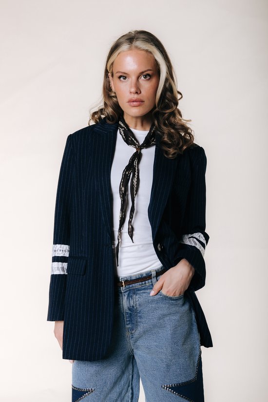 Model draagt een donkerblauwe krijtstreepp blazer, wit T-shirt, jeans en een sjaal met print.