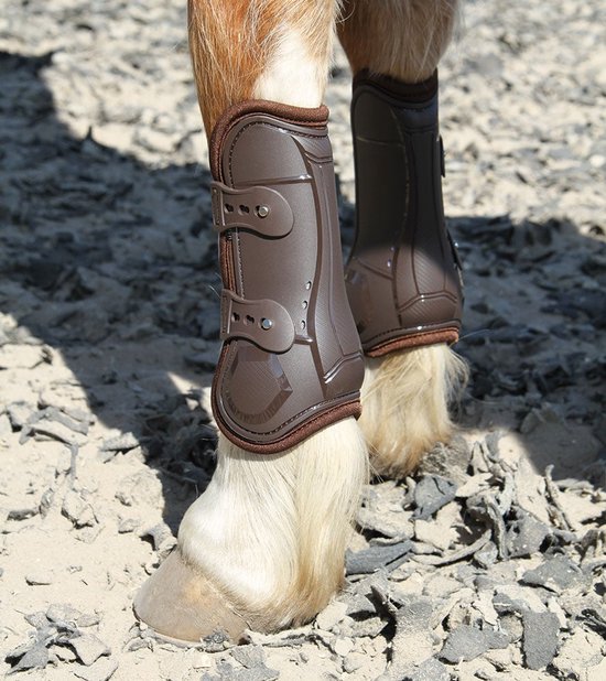 Bruine peesbeschermers met klittenbandsluitingen, gedragen door een paard op een zanderige ondergrond.