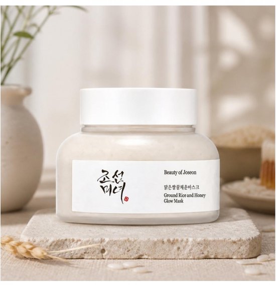 Beauty of Joseon Ground Rice and Honey Glow Mask in een potje, op een stenen onderzetter, met rijst en tarwe op de achtergrond.