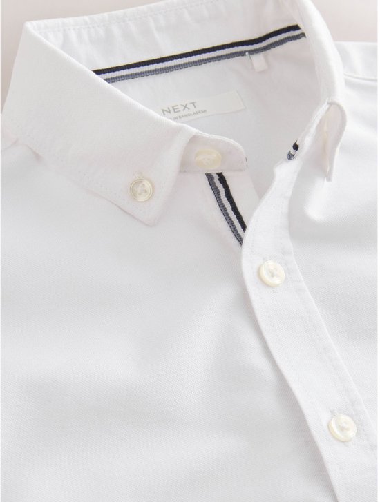 Detail van de kraag van een wit Oxford overhemd met blauw-witte strepen aan de binnenkant en knoopjes.
