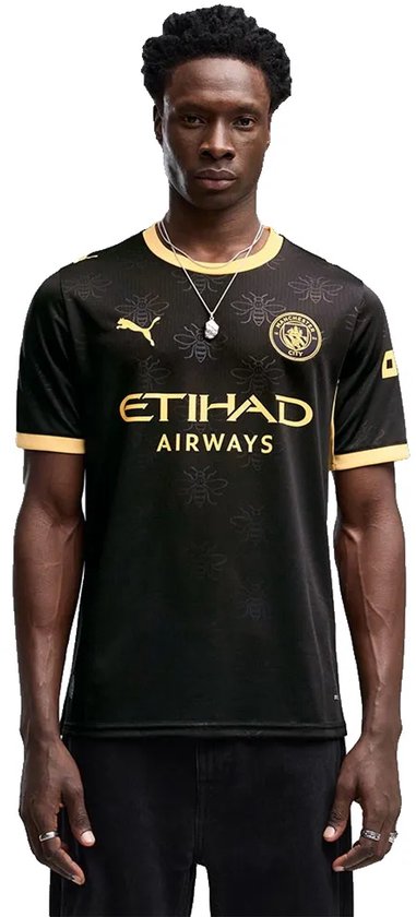 Man draagt zwart replica voetbalshirt met gouden 'ETIHAD AIRWAYS' logo, bijenprint en gouden kraag.