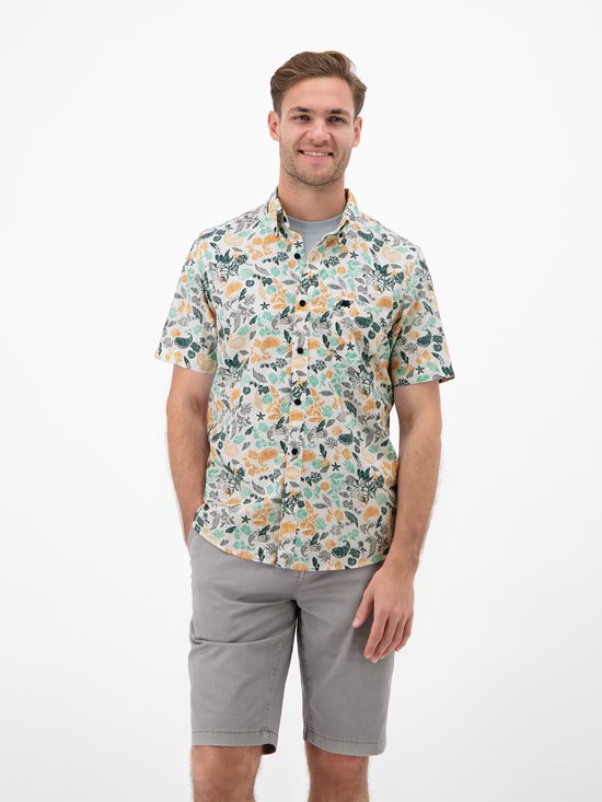 Model van voren, lachend, in wit overhemd met print van vissen, schelpen en zeewier in groen, oranje en geel.