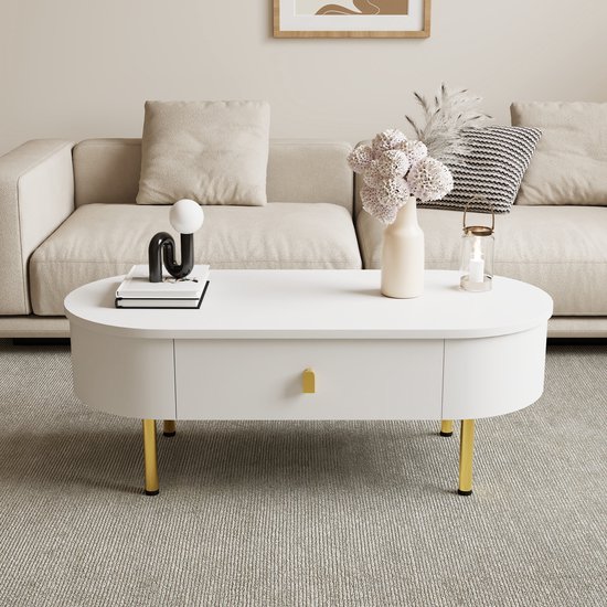 Witte ovale salontafel met twee lades, gouden poten en handgrepen, geplaatst voor een beige bank.