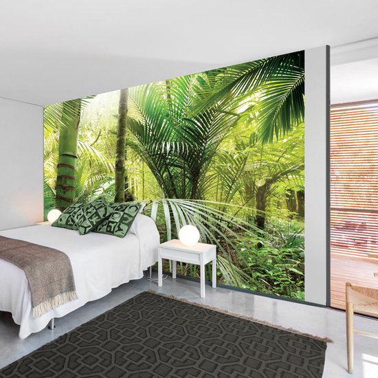 Une chambre avec une peinture murale de jungle verte donnant sur un lit avec des draps blancs et des oreillers verts.