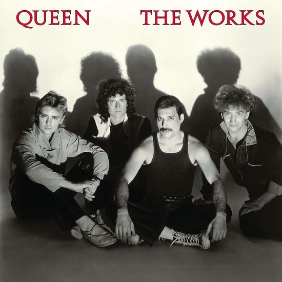 Queen bandleden zitten op de grond, met 'QUEEN THE WORKS' boven hen.