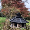Houten vogelhuisje met donker dak en schoorsteen, in herfsttuin.