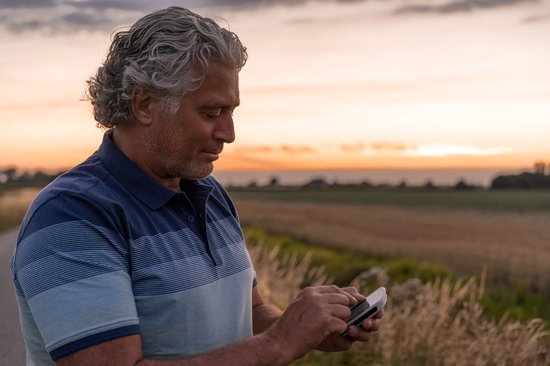 Man met grijze haren gebruikt Garmin fietsnavigatie bij zonsondergang.
