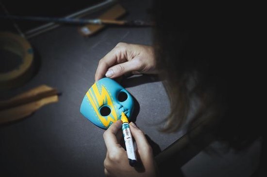 Hand tekent gele lijnen op blauw masker met stift. Donkere achtergrond.
