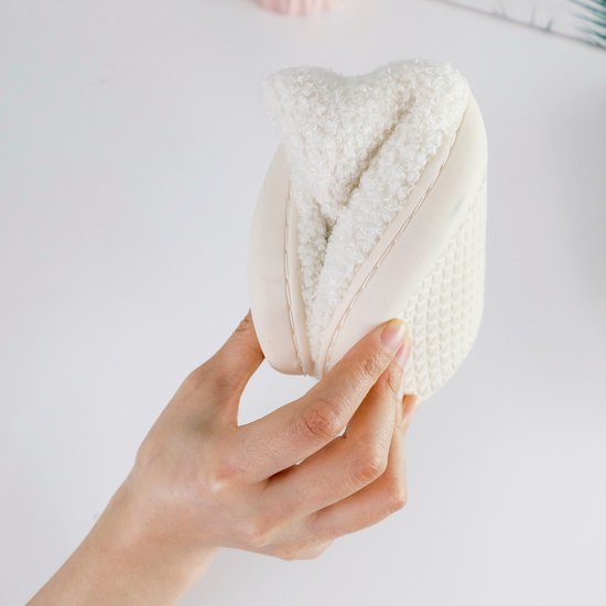 Witte fuzzy pantoffel, in de hand gehouden, de zool is zichtbaar.