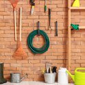 Een groene tuinslang hangt opgerold aan een bakstenen muur, naast tuingereedschap.