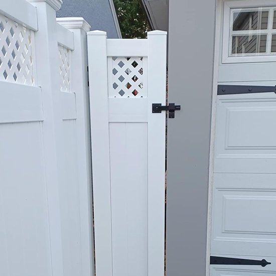 Zwarte poortsluiting op een wit tuinhek naast een garage.