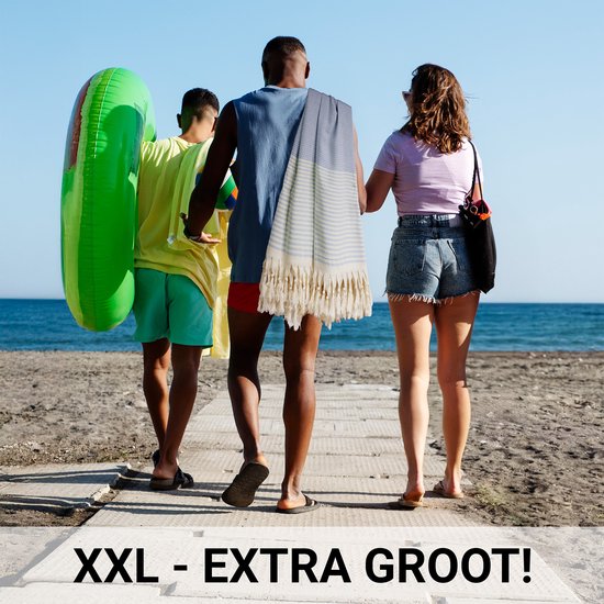 Drie personen lopen over een strand, met een opblaasbare groene ring en een grote gestreepte handdoek.