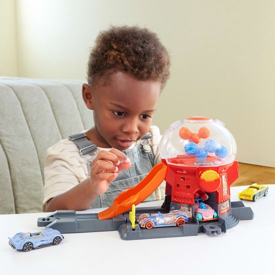 Jongen speelt met rode Hot Wheels snoepautomaat speelset, auto's en glijbaan