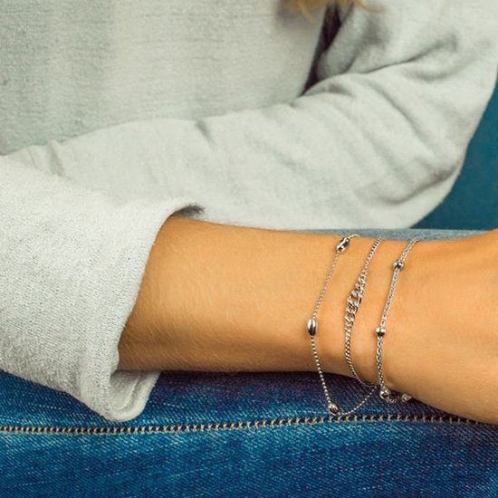 Twee zilverkleurige armbanden om een arm. Eén met ovale schakels en bolletjes, de andere met een fijne ketting met bolletjes.
