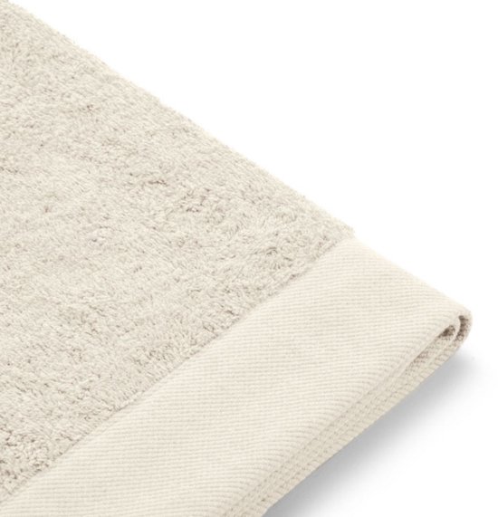 Close-up van de beige badstof en de brede, lichte beige band aan de rand van de handdoek.