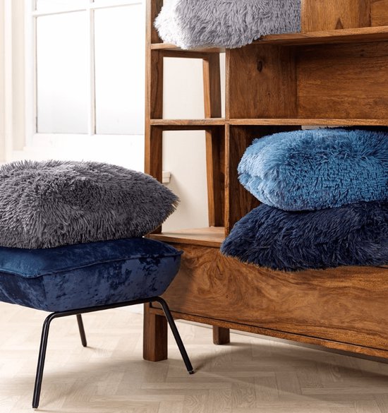 Grijze en blauwe pluizige kussens op een houten kast en een krukje met metalen pootjes.