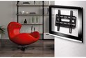 Zwarte TV-muurbeugel gemonteerd op een gestructureerde muur, naast een rode fauteuil.