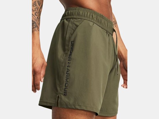 Legergroene shorts met verticale zwarte Under Armour-letters op de linkerpijp