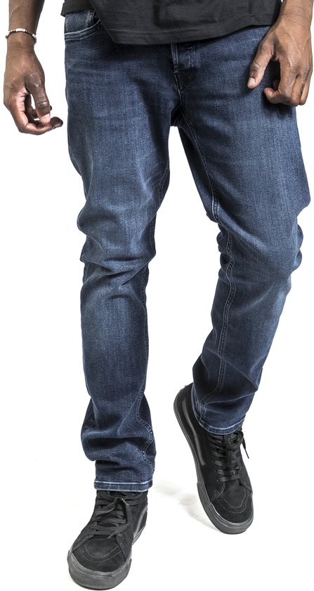 De voorkant van een man in een donkerblauwe jeans, met zwarte Vans schoenen.