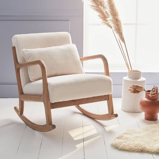 Schommelstoel met een licht houten frame en crème bouclé bekleding, in een lichte kamer met decoratie.