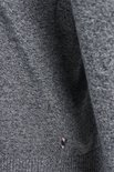 Gedetailleerd beeld van een grijze gebreide trui met een klein logo op de heup.