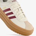 Detail van de neus van een witte damessneaker met beige suède en bordeauxrode Adidas-strepen op de dikke bruine plateauzool.