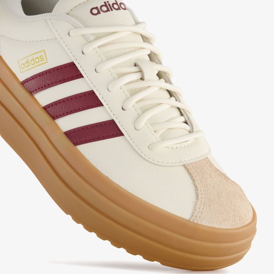 Detail van de neus van een witte damessneaker met beige suède en bordeauxrode Adidas-strepen op de dikke bruine plateauzool.