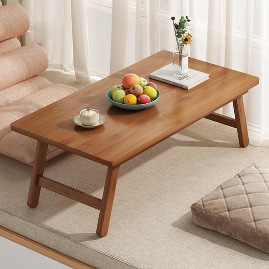 Een bamboe klaptafel bij een raam, met fruit, een kopje en een boek.