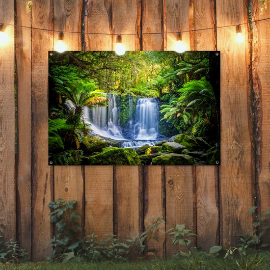 Waterval in een groen bos, met varens en mos, aan een houten schutting.