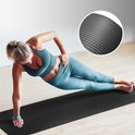 Vrouw in blauwgroene sportkleding doet zijwaartse plank op zwarte fitnessmat. Inzetstuk toont profiel.