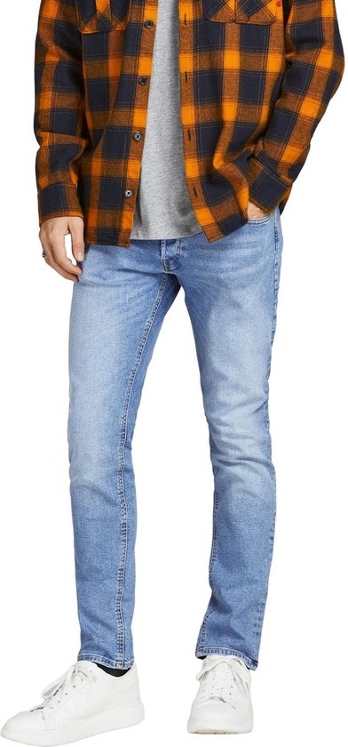 Man draagt een lichtblauwe skinny jeans met een oranje met zwart geblokt overhemd en grijze top.