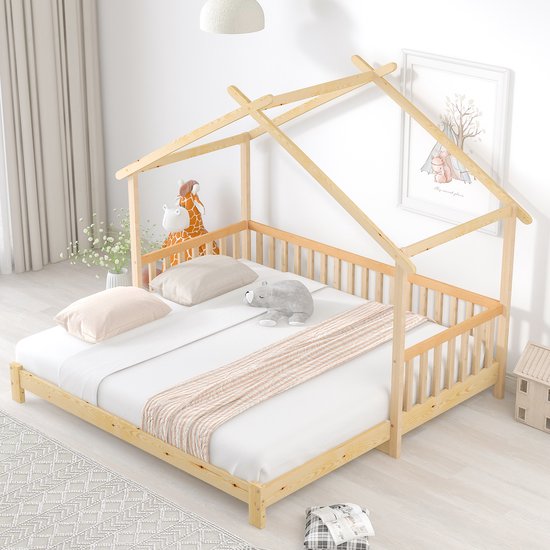 Houten huisbed met spijlen en matras, versierd met knuffels en een deken, in een kinderkamer met een print aan de muur.