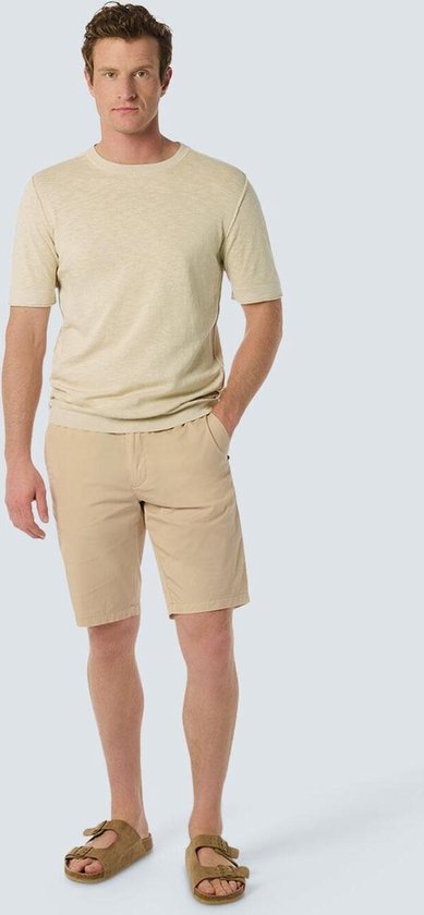Homme en t-shirt beige et short beige, portant des sandales.